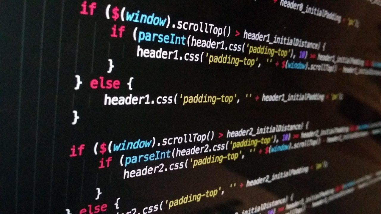 A developer types code on a laptop at a desk with multiple monitors displaying terminal windows.