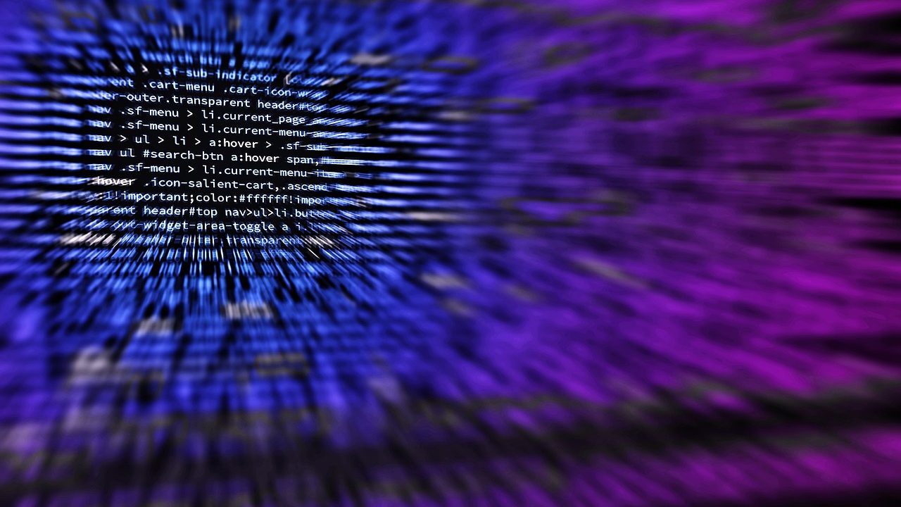 Hands typing on a mechanical keyboard in front of multiple monitors showing code.