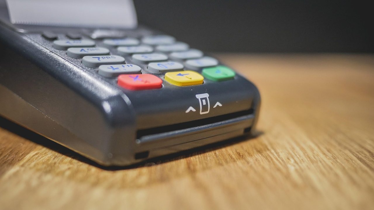 A contactless payment terminal on a retail counter with a card being tapped.