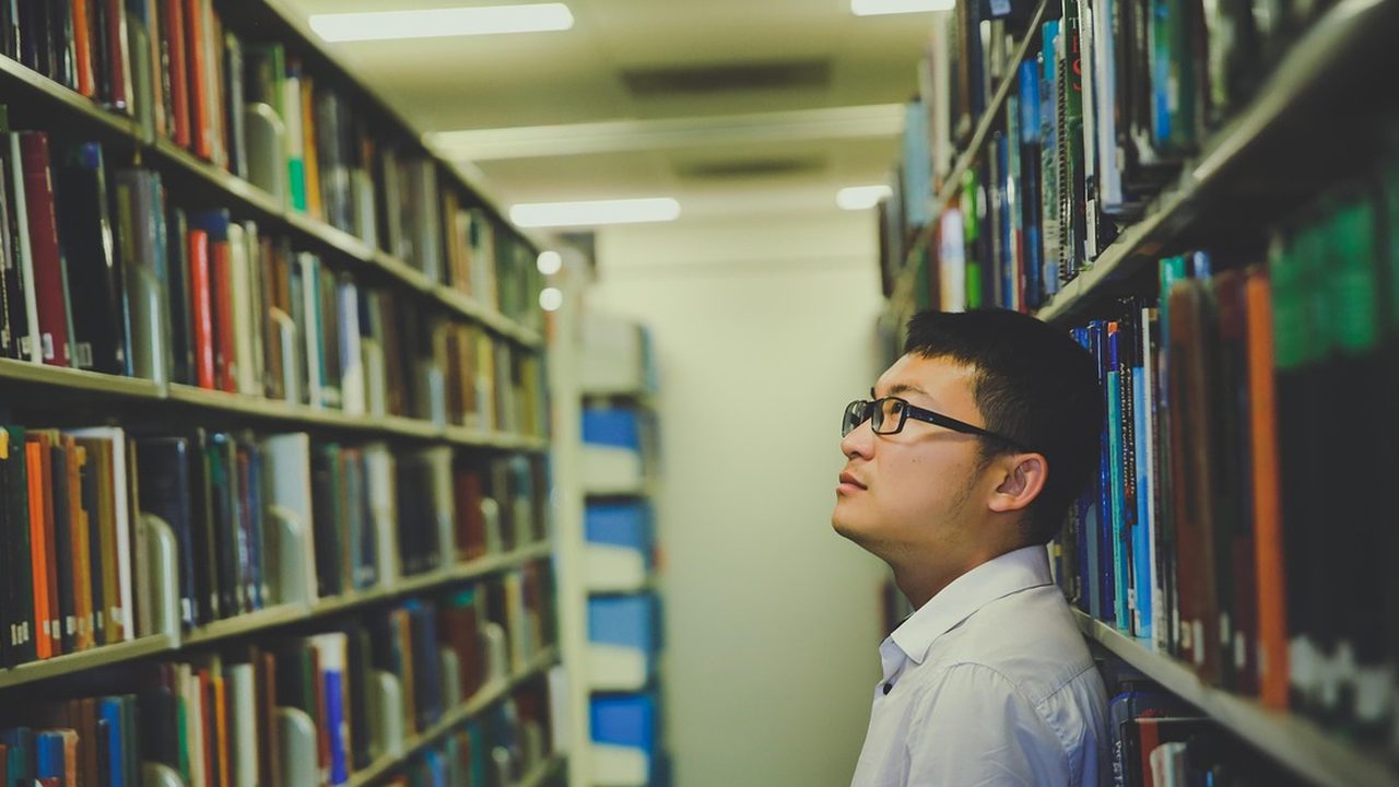 Rows of wooden desks and shelves of books inside a quiet university library reading room.