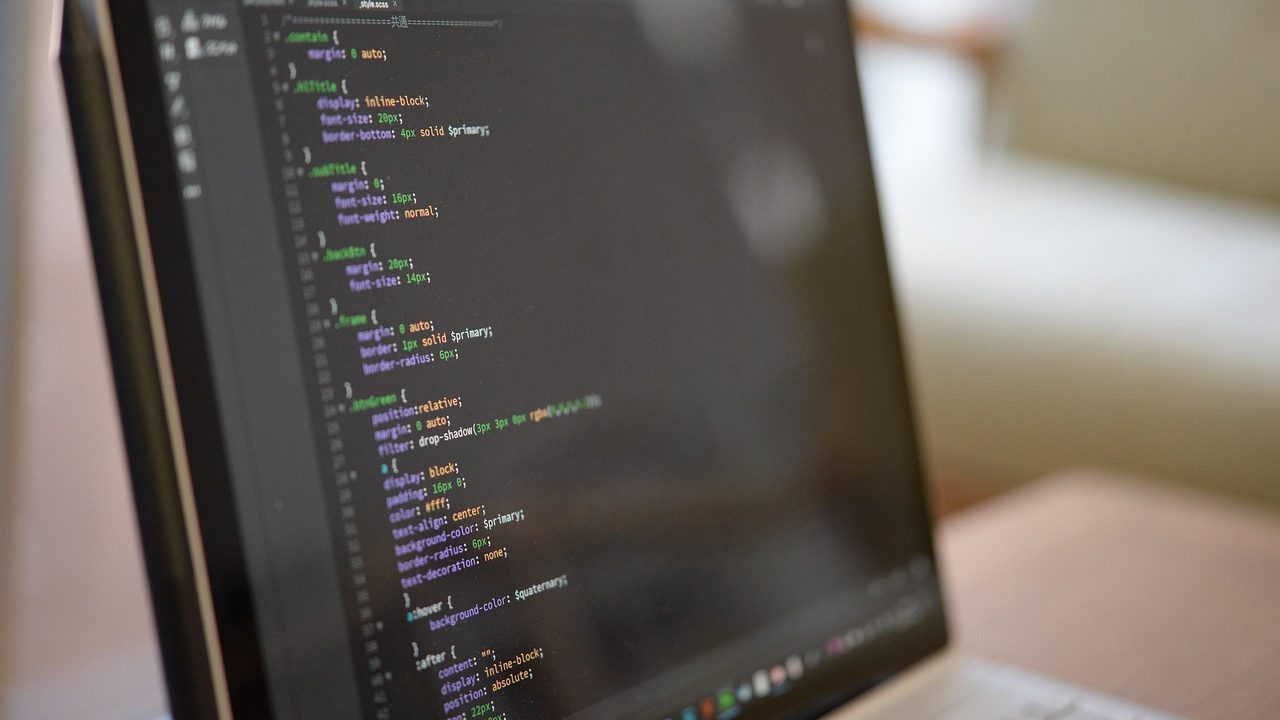 A developer's hands typing on a laptop with lines of code visible on the screen.