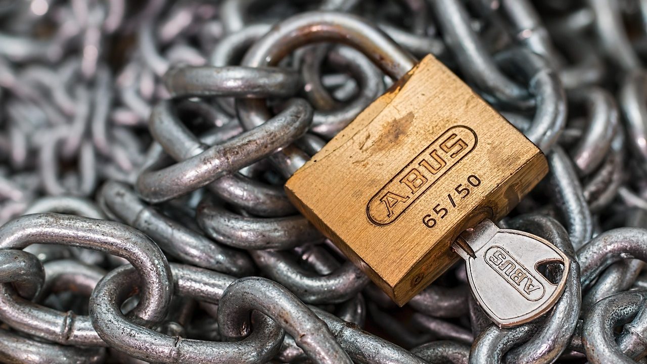 Close-up of a padlock resting on a keyboard in front of glowing server indicator lights.