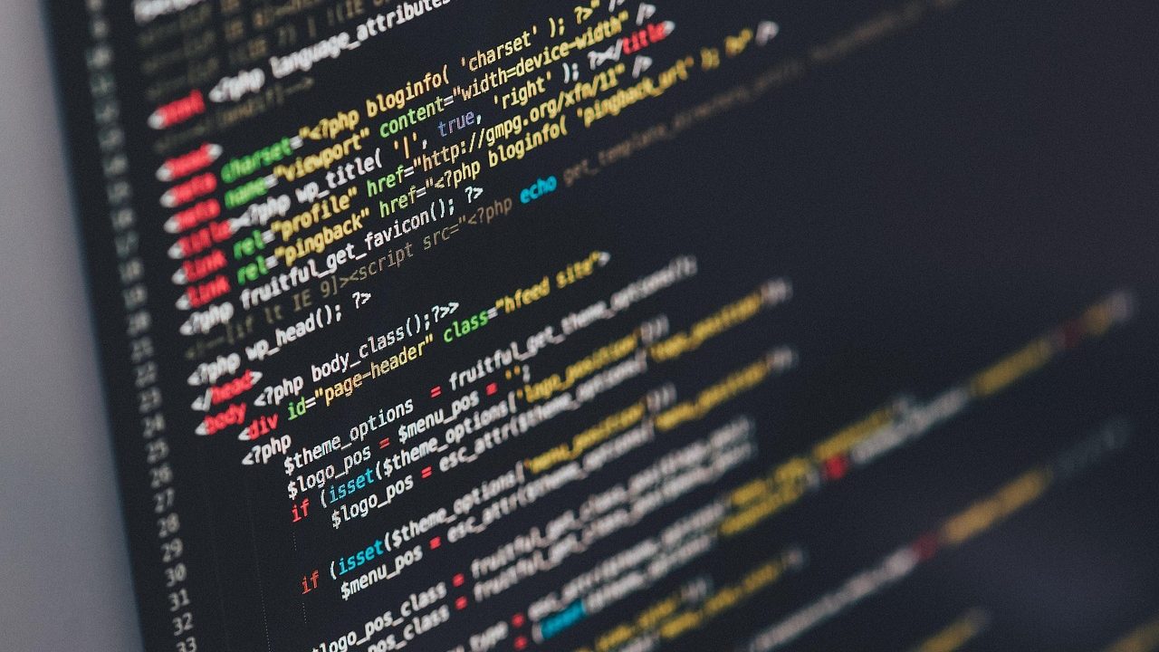 A glowing laptop screen displays lines of code in a dimly lit workspace.