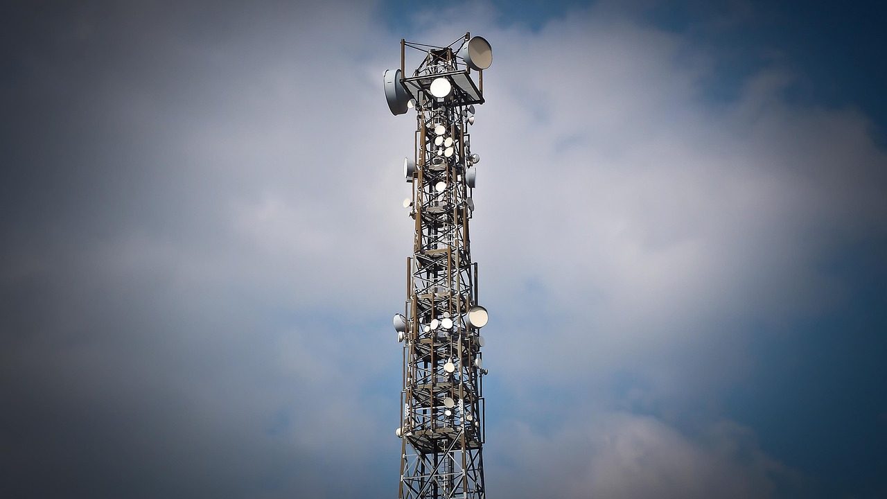 A tall shortwave radio antenna tower stands against an open sky at dusk.