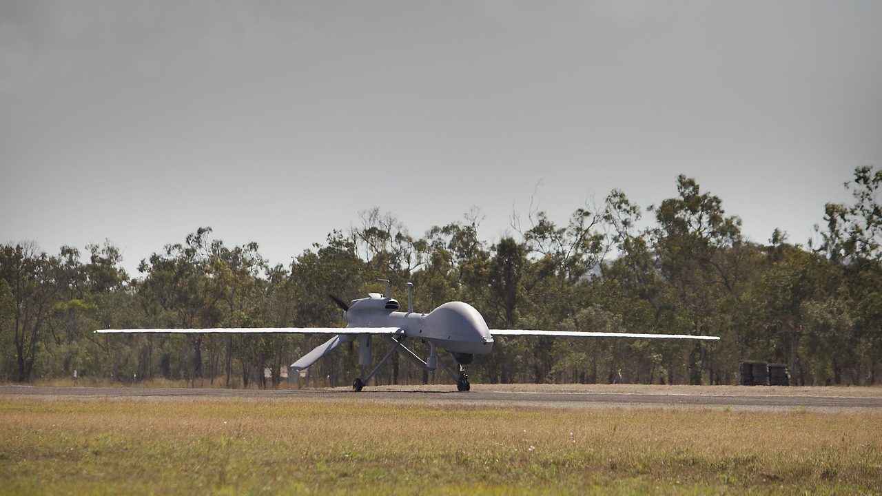 An unmanned military drone sits on a tarmac runway.
