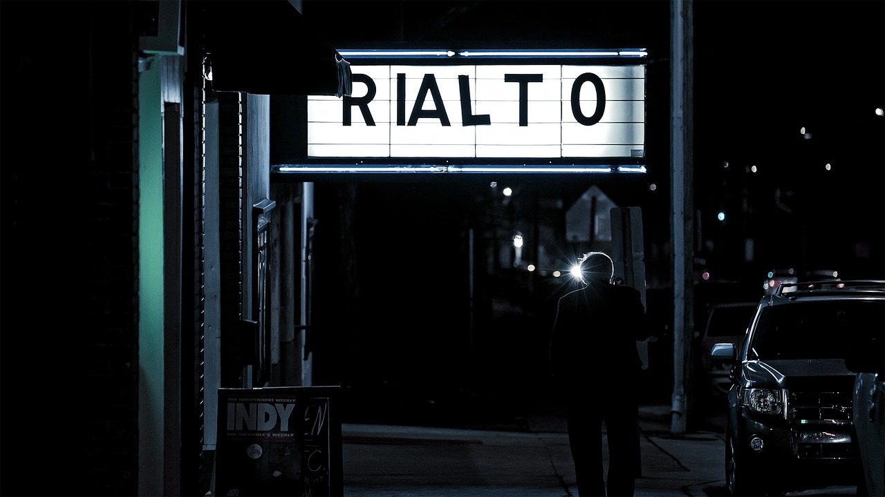 A glowing movie theater marquee lit up at night outside a cinema entrance.