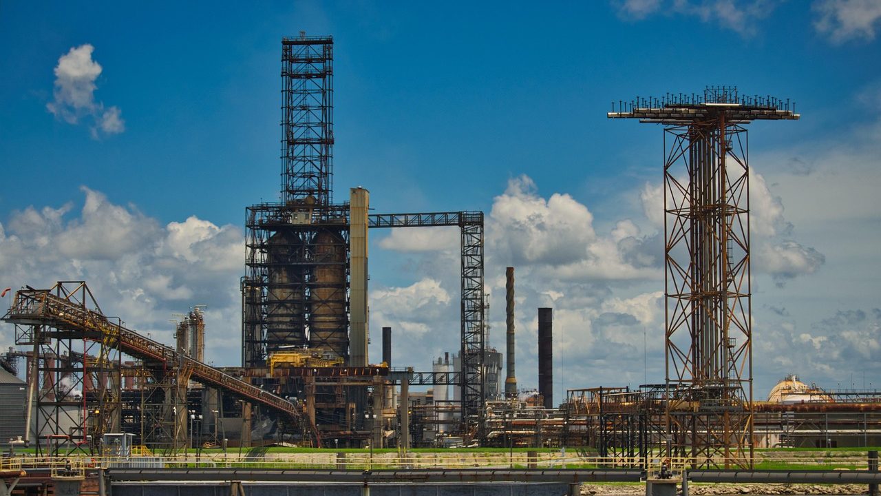 Industrial oil refinery towers emit steam against a twilight sky.