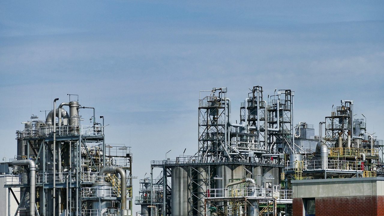 Industrial oil refinery towers illuminated at night with smoke rising against a dark sky.