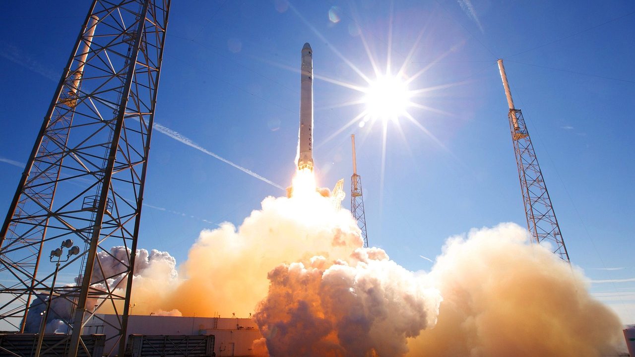 A tall rocket on a launch pad gantry against a clear blue sky before liftoff.