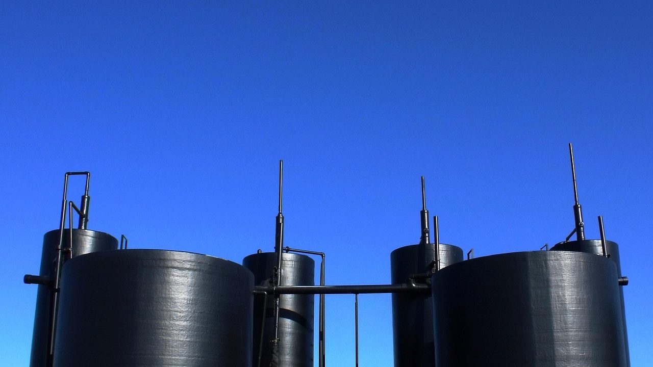 Large cylindrical petroleum storage tanks at an industrial oil depot under a pale sky.