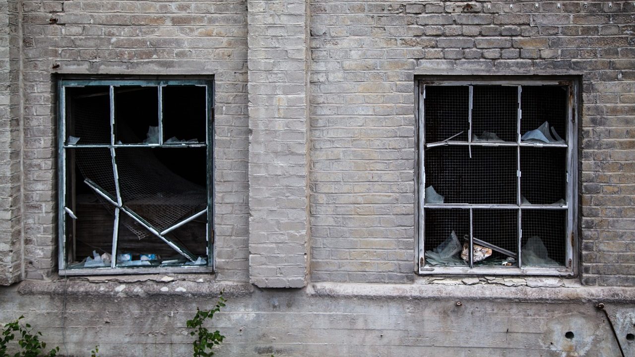 An industrial factory exterior shows signs of structural damage and smoke.