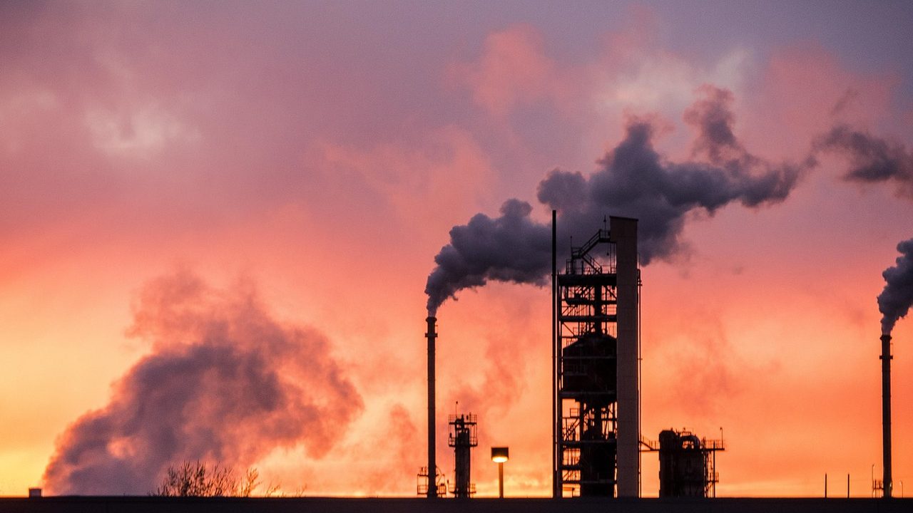 A large oil refinery with a network of silver pipes and towers against a cloudy sky.