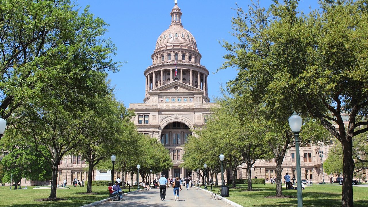 A classical state capitol building with white columns under a bright blue sky.