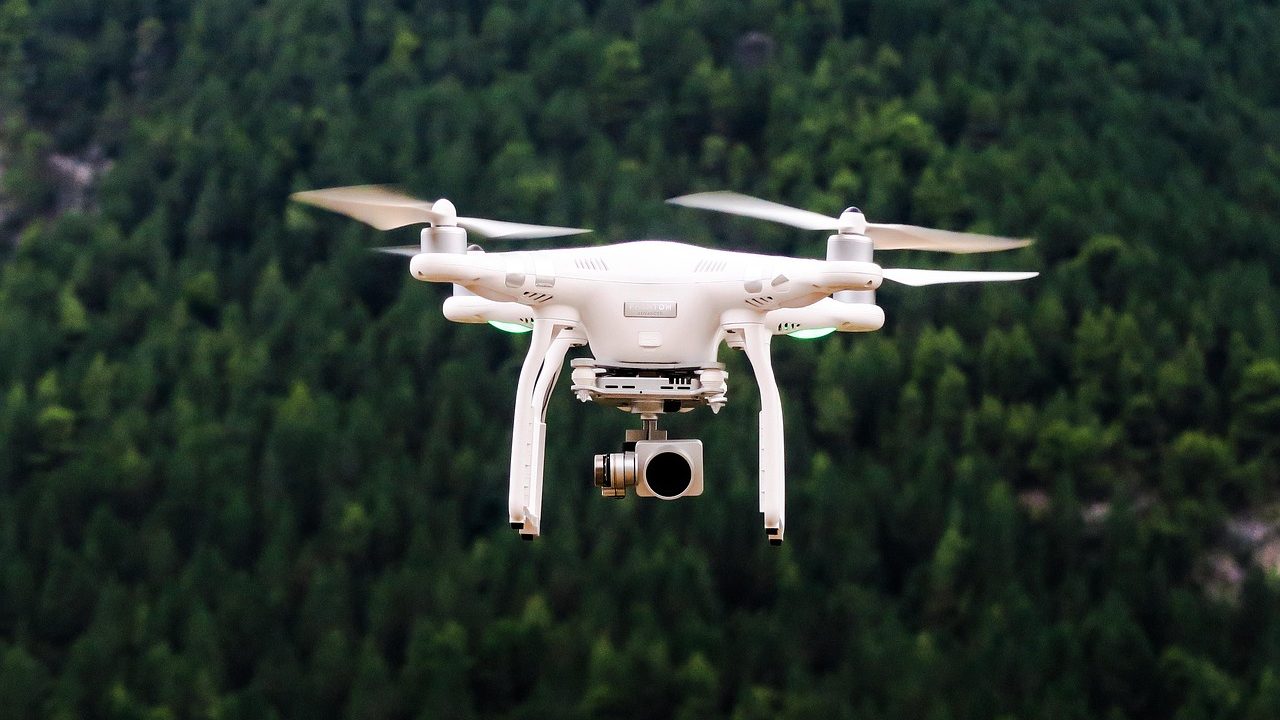 A small unmanned aerial drone in flight against a pale blue sky.