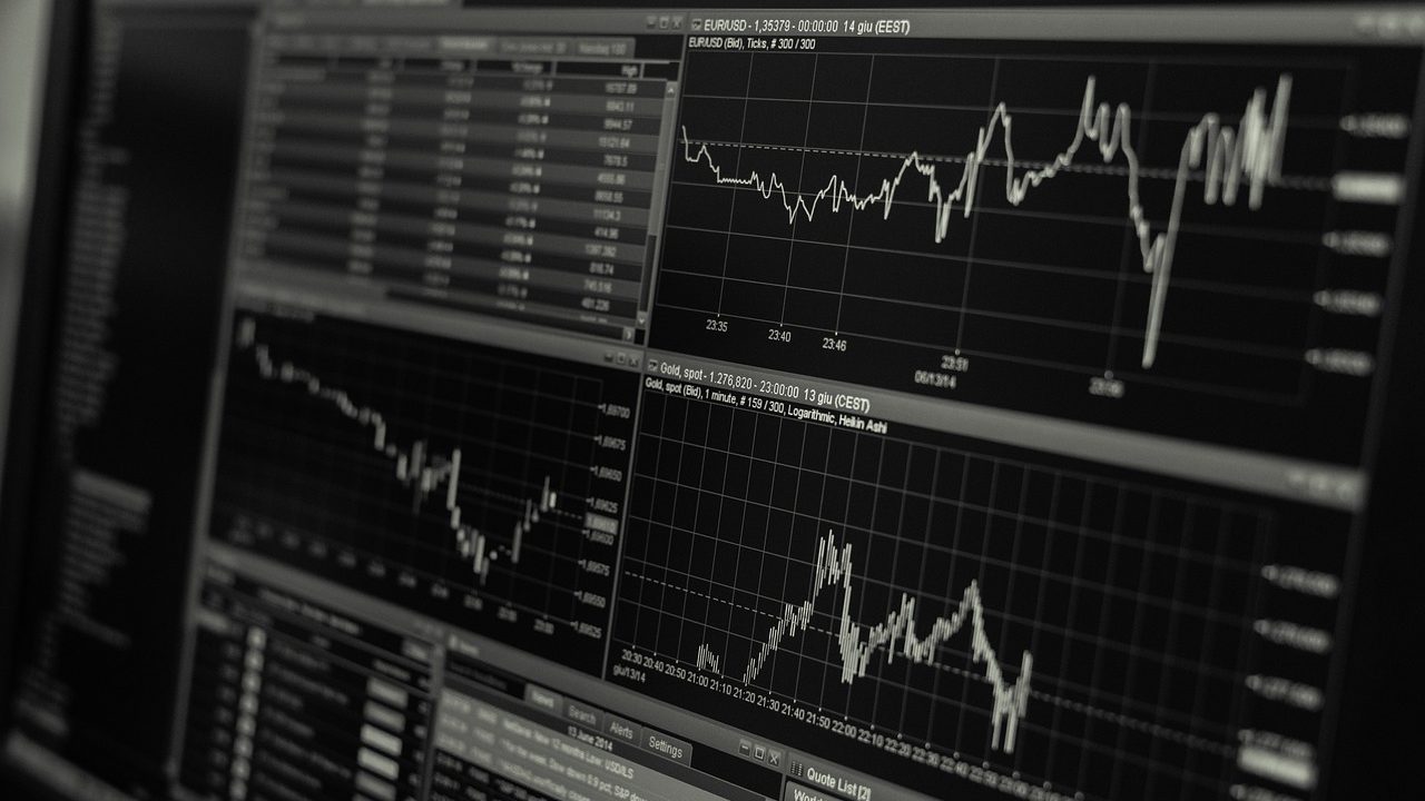 Traders at workstations surrounded by multiple monitors displaying financial charts on a busy exchange floor.