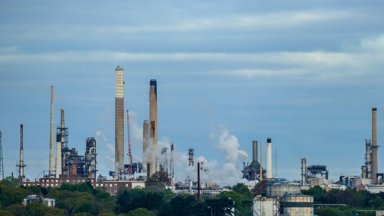 A large oil refinery complex with pipes, towers, and industrial infrastructure photographed from ground level.