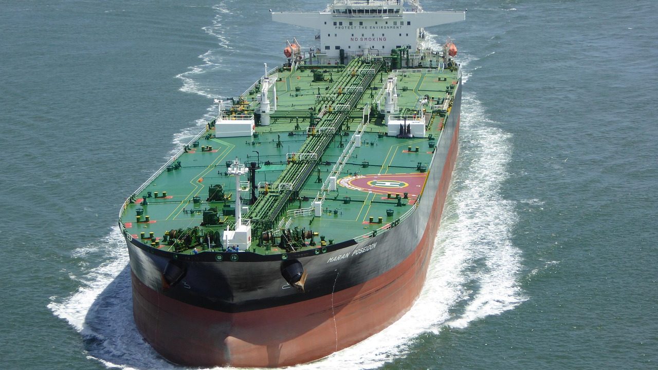 A large oil tanker moves through calm blue open water under a clear sky.