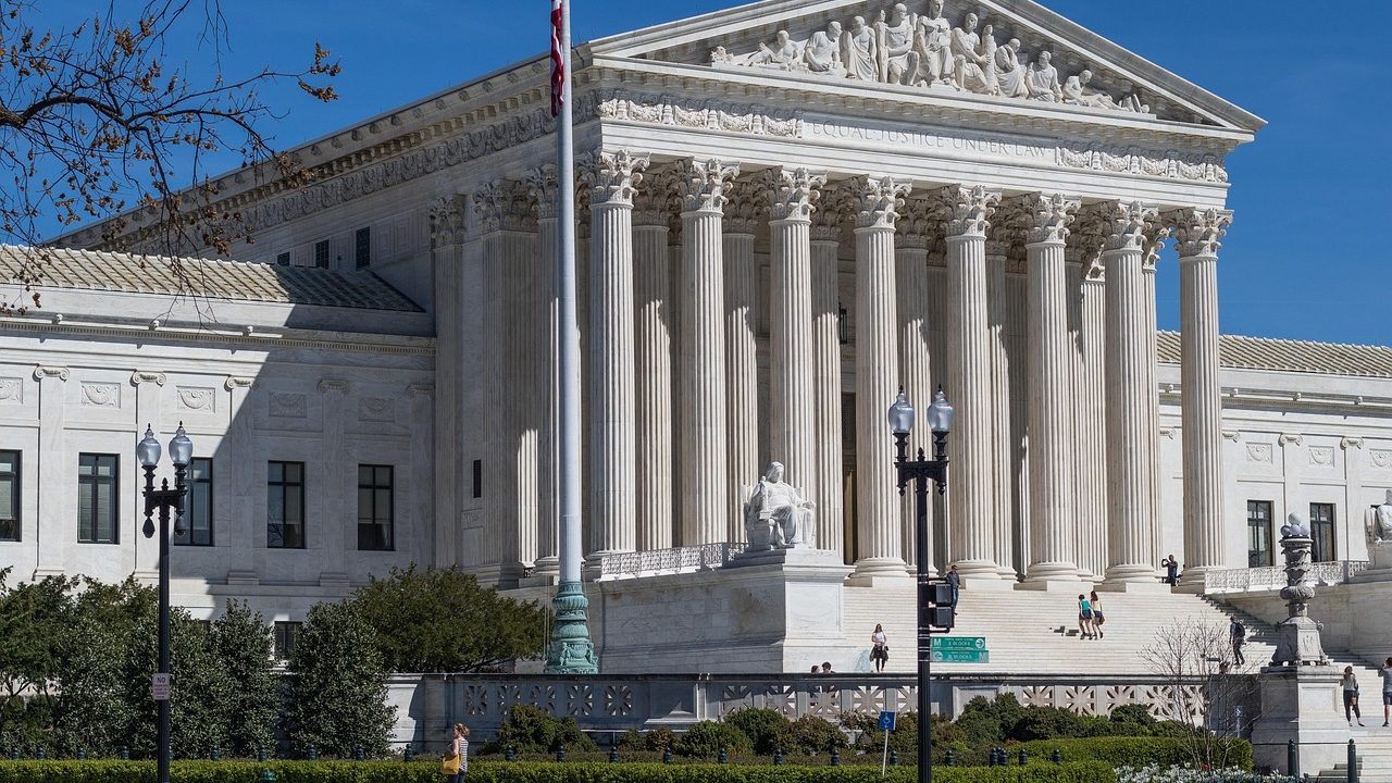 The white marble columns and steps of a neoclassical courthouse facade in daylight.
