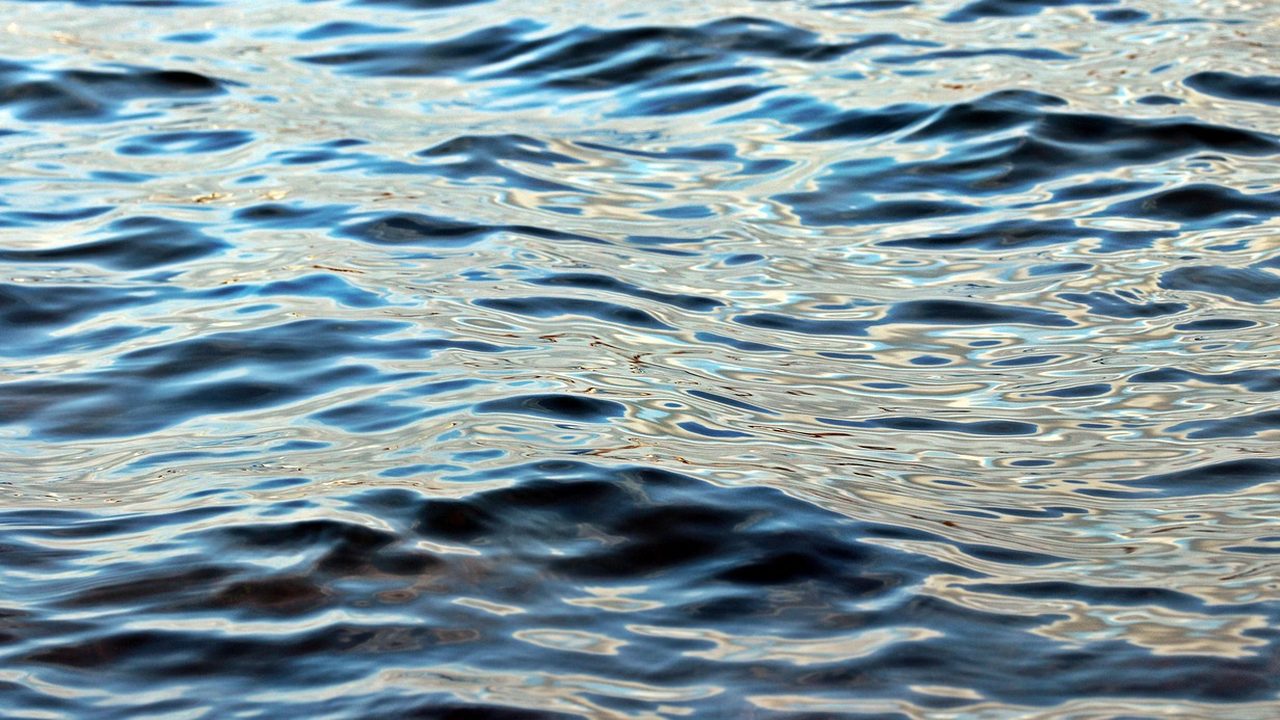 A wide aerial view of the open ocean surface under a bright sky.