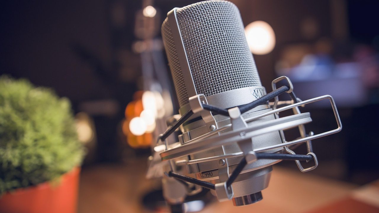 A professional condenser microphone in a dimly lit recording studio booth.