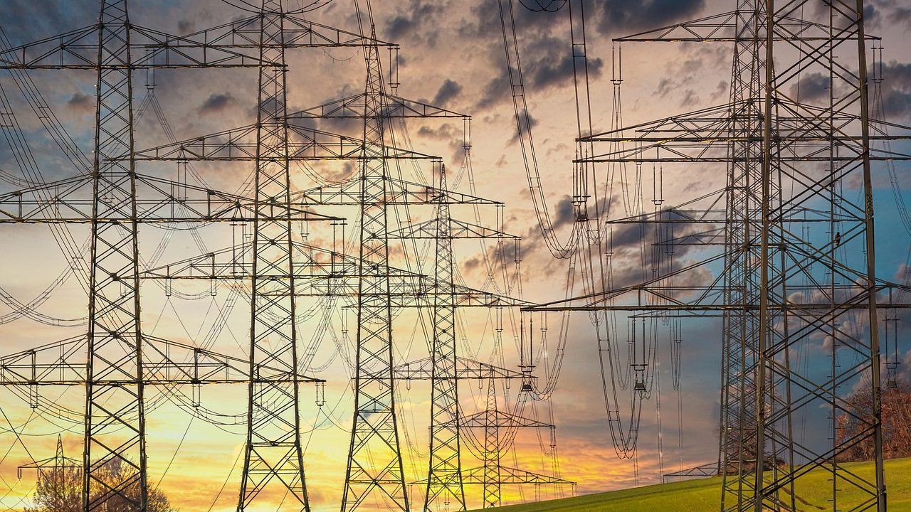 High-voltage electrical transmission towers and lines shimmering under intense summer heat.