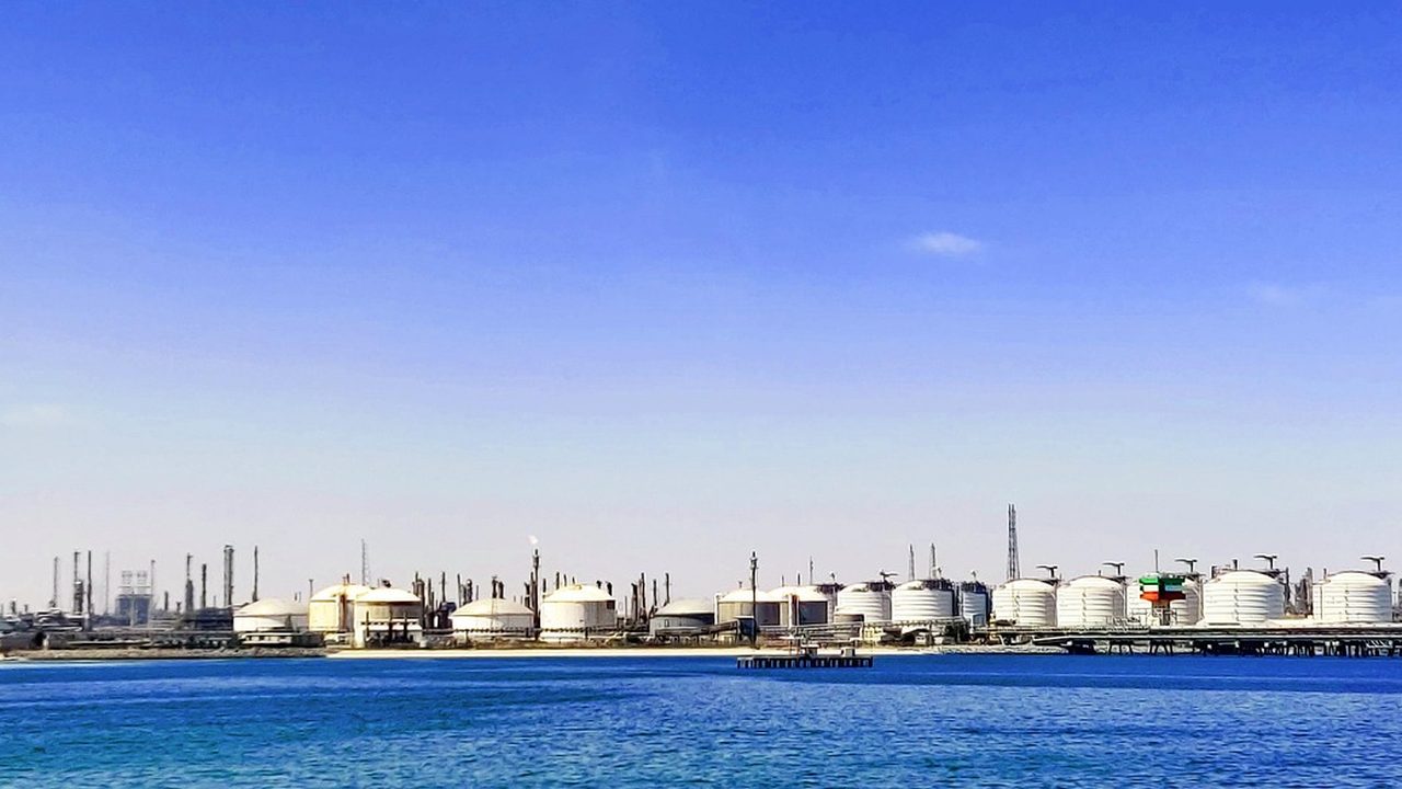 Towers and pipes of a large oil refinery complex rise against a gray industrial sky.