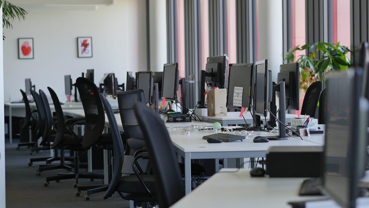 A row of empty office desks with computers in a modern open-plan workspace.