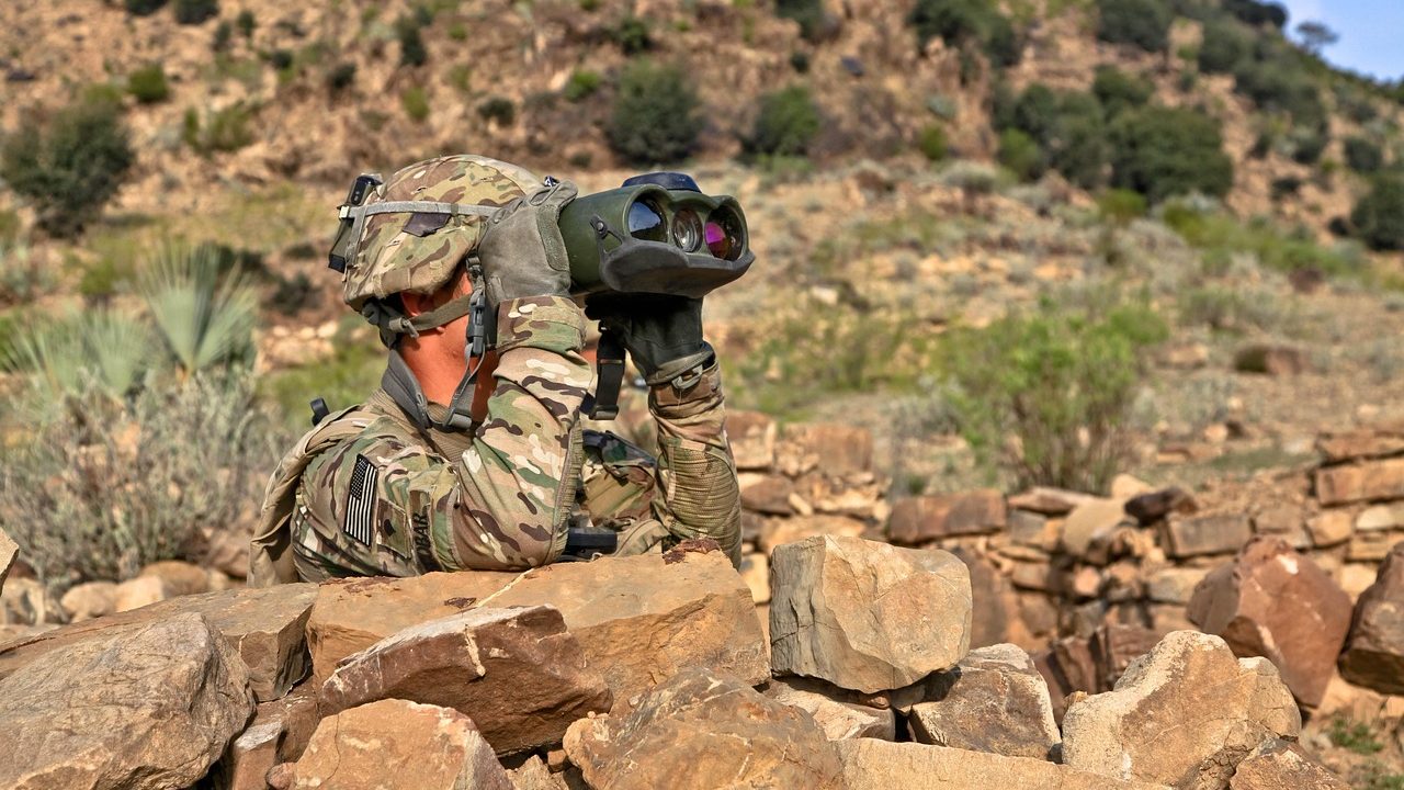 A military-style unmanned aerial drone sitting on an open field with operators nearby.