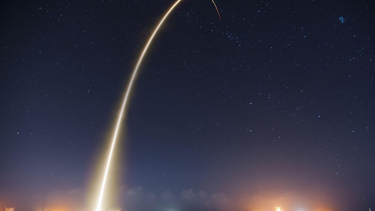 A large rocket on a illuminated launch pad at night with steam venting from the base.