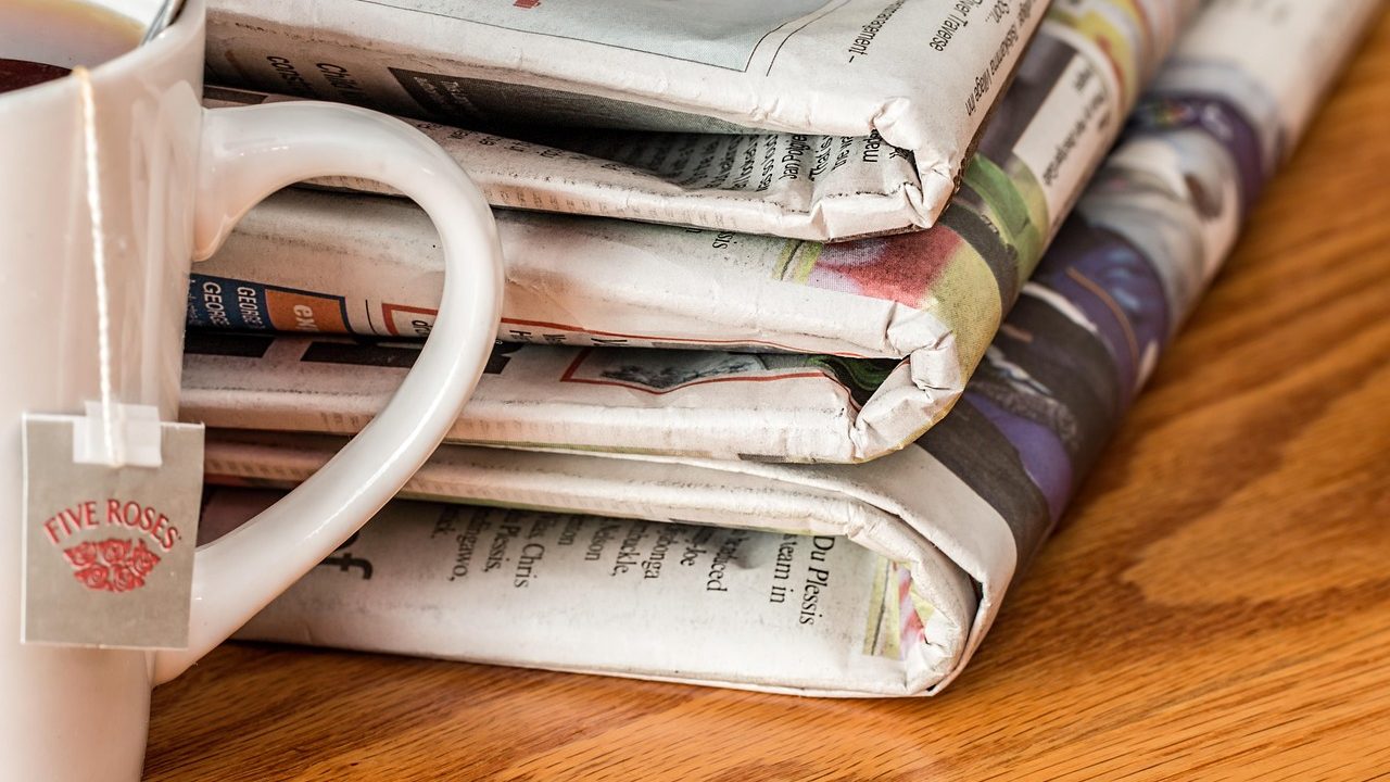 Rolls of newspaper moving through a large commercial printing press in a production facility.