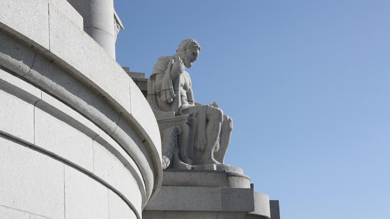 The stone facade and dome of a state capitol building against a partly cloudy sky.