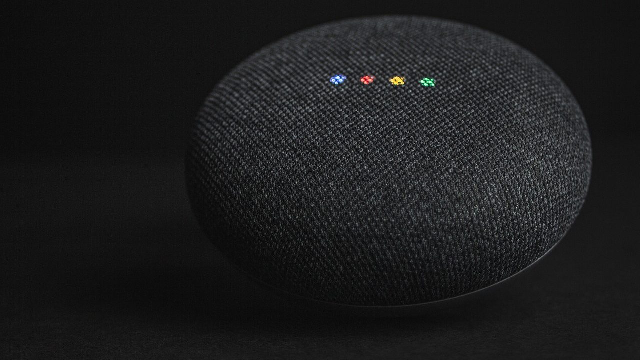 A cylindrical smart speaker device on a wooden desk with soft ambient lighting.