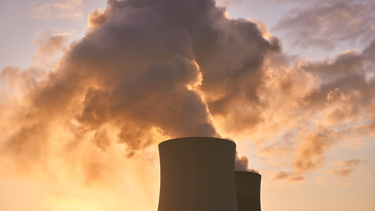 Large concrete cooling towers of a nuclear power plant rise against an overcast sky.