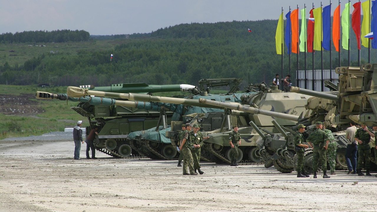 A convoy of military tanks moving along a wide road in overcast conditions.