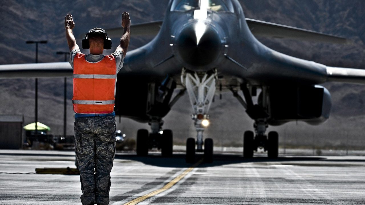 Fighter jets parked on a tarmac at a desert military air base under a pale sky.