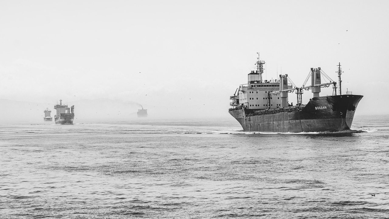 A bulk cargo freighter navigating rough gray sea water under heavy clouds.