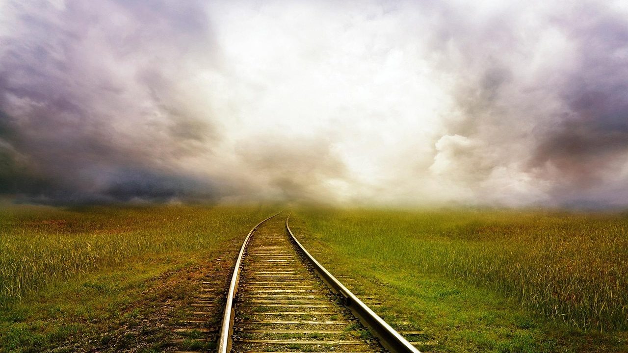 Long straight railroad tracks stretching toward the horizon through open countryside at dusk.