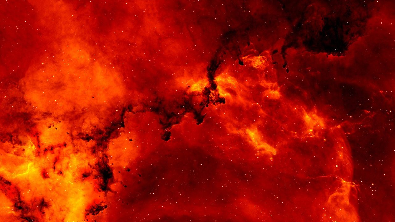 A colorful infrared space telescope image showing glowing gas and dust clouds forming a nebula.