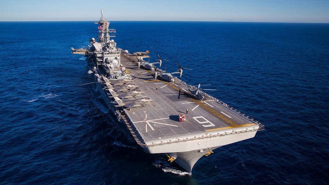 A large aircraft carrier steaming across open ocean under a blue sky.