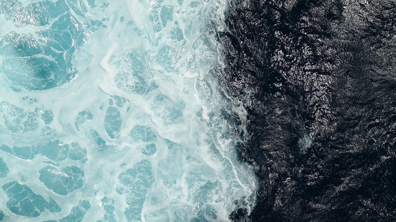 Aerial view of a vast open ocean surface with gentle wave patterns under a clear sky.