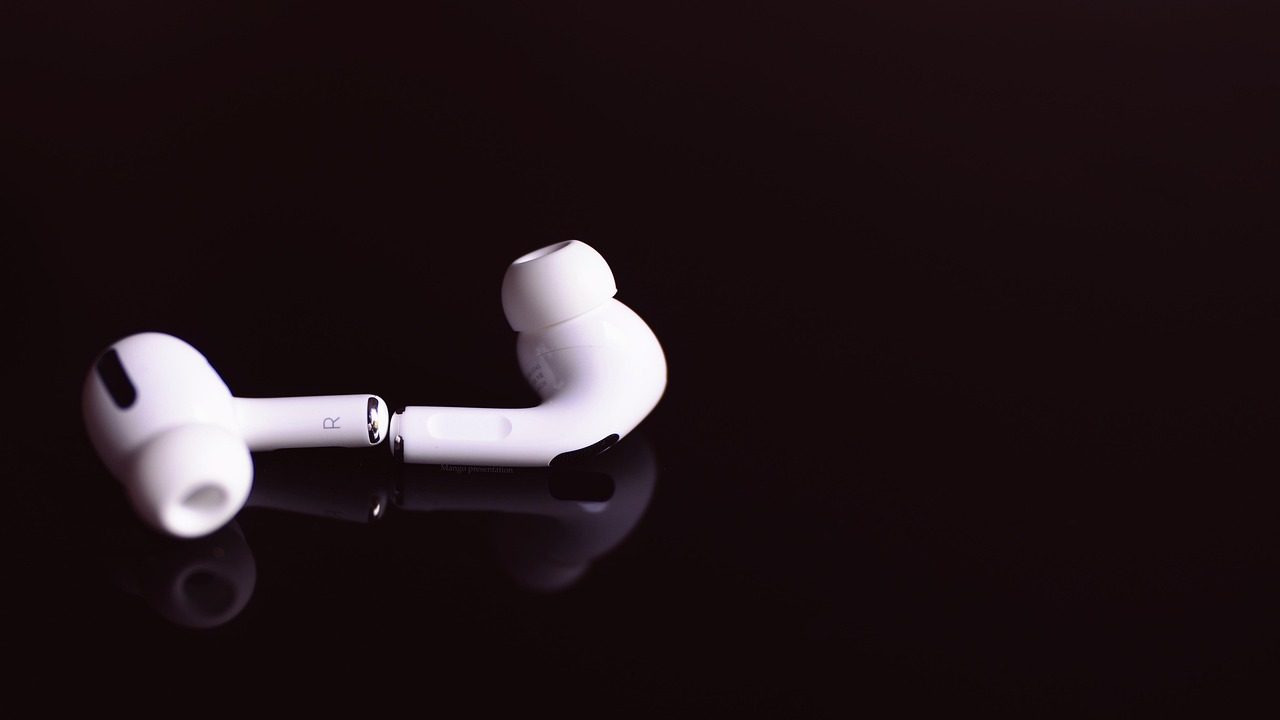 A pair of white wireless earbuds rests on a reflective surface against a light background.