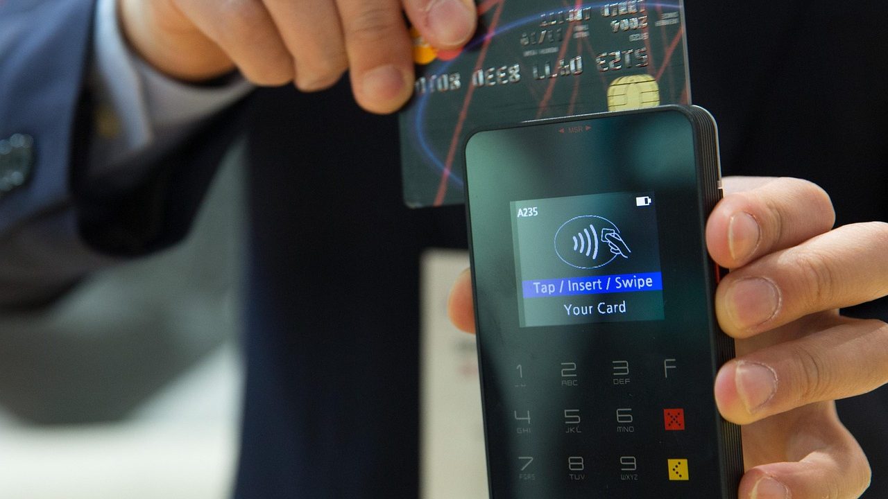 A customer tapping a credit card on a sleek payment terminal at a retail counter.