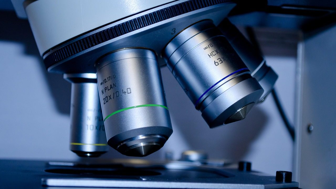 A scientist examines a small sample under a high-powered microscope in a clean laboratory setting.
