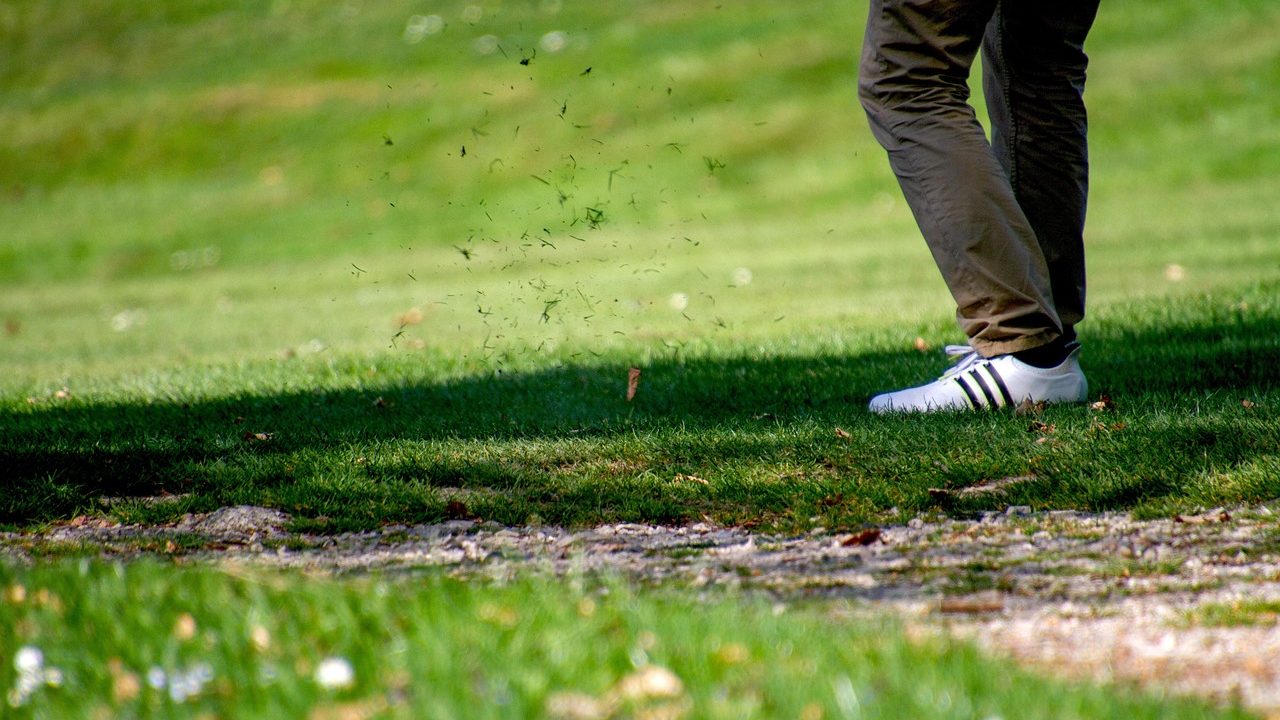 A manicured golf course fairway stretching toward a green flag under afternoon sunlight.