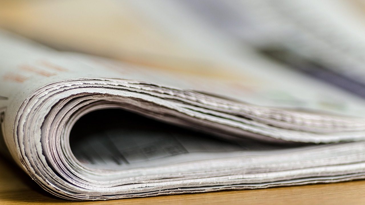 Rolls of paper moving through a large commercial printing press in a newspaper facility.