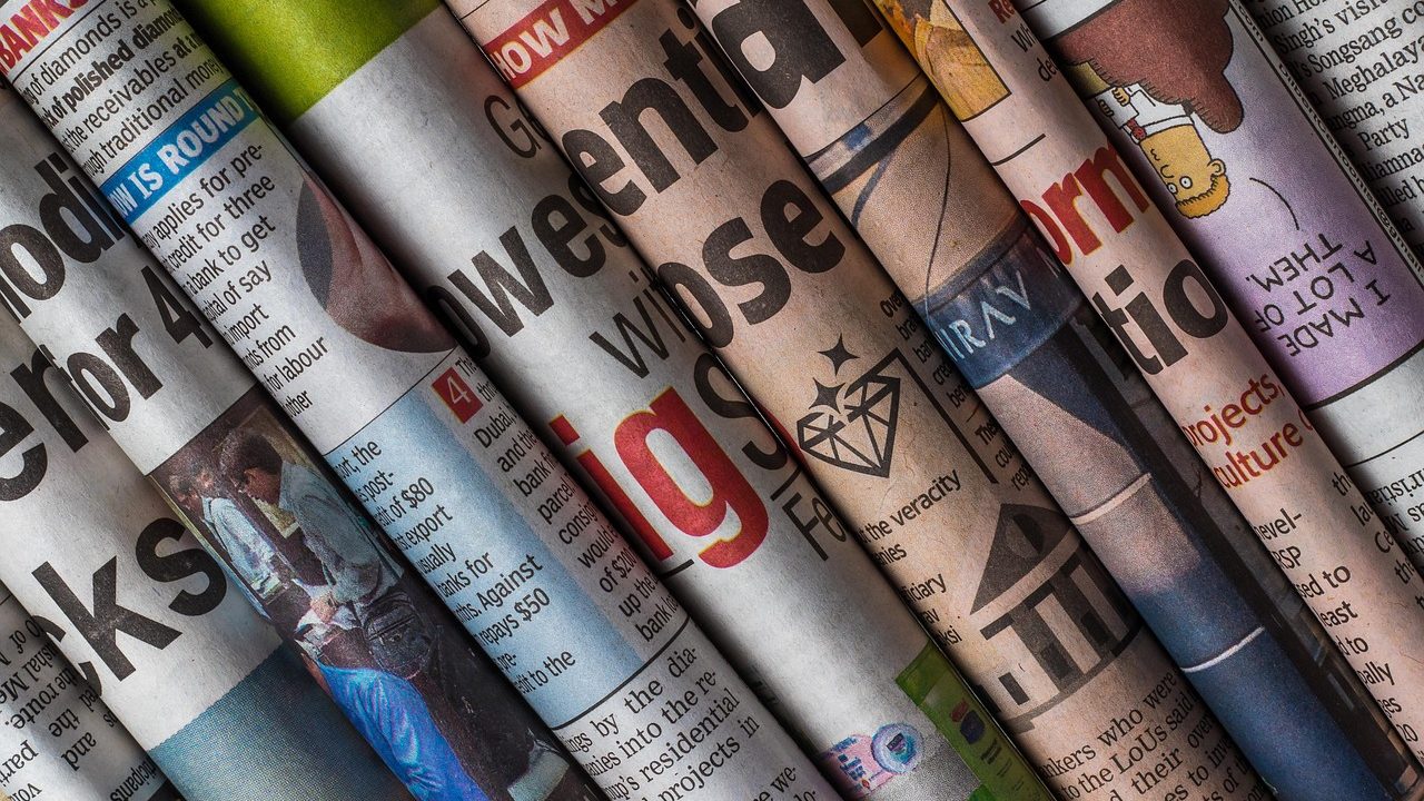 Rolls of newsprint feed through a large commercial printing press in a production facility.
