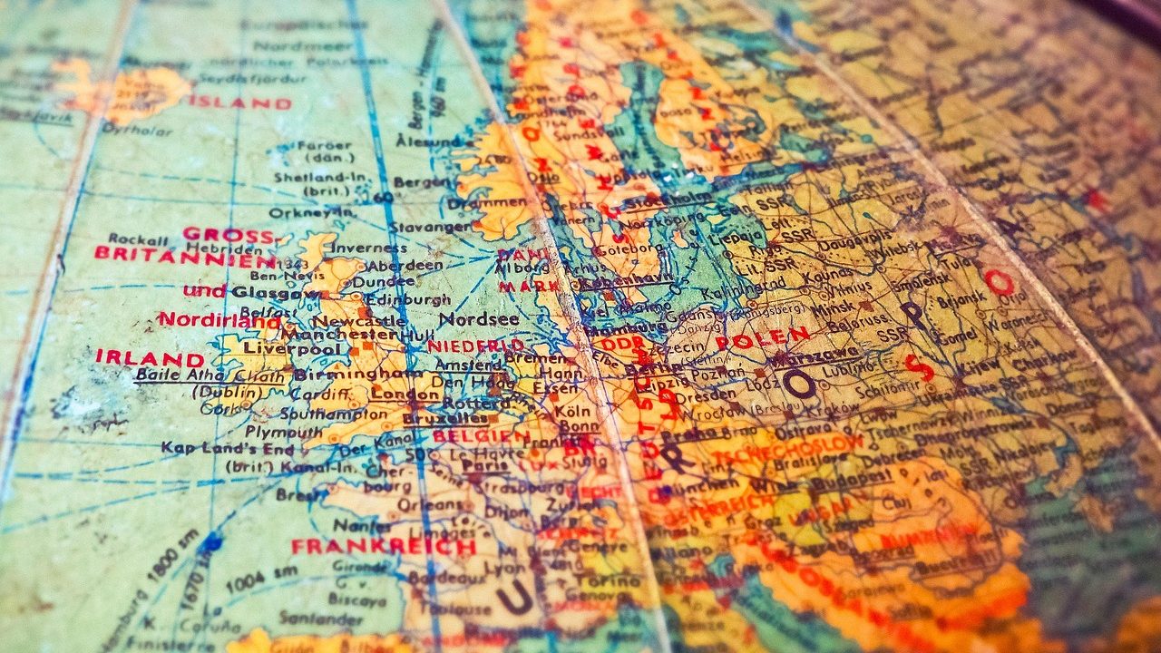 A detailed physical globe sits on a wooden desk beside an open atlas showing geographic features.