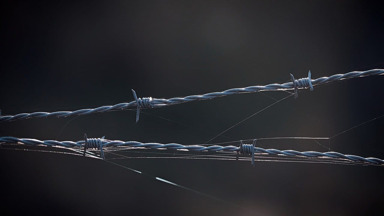 A steel border fence stretching across open desert landscape.