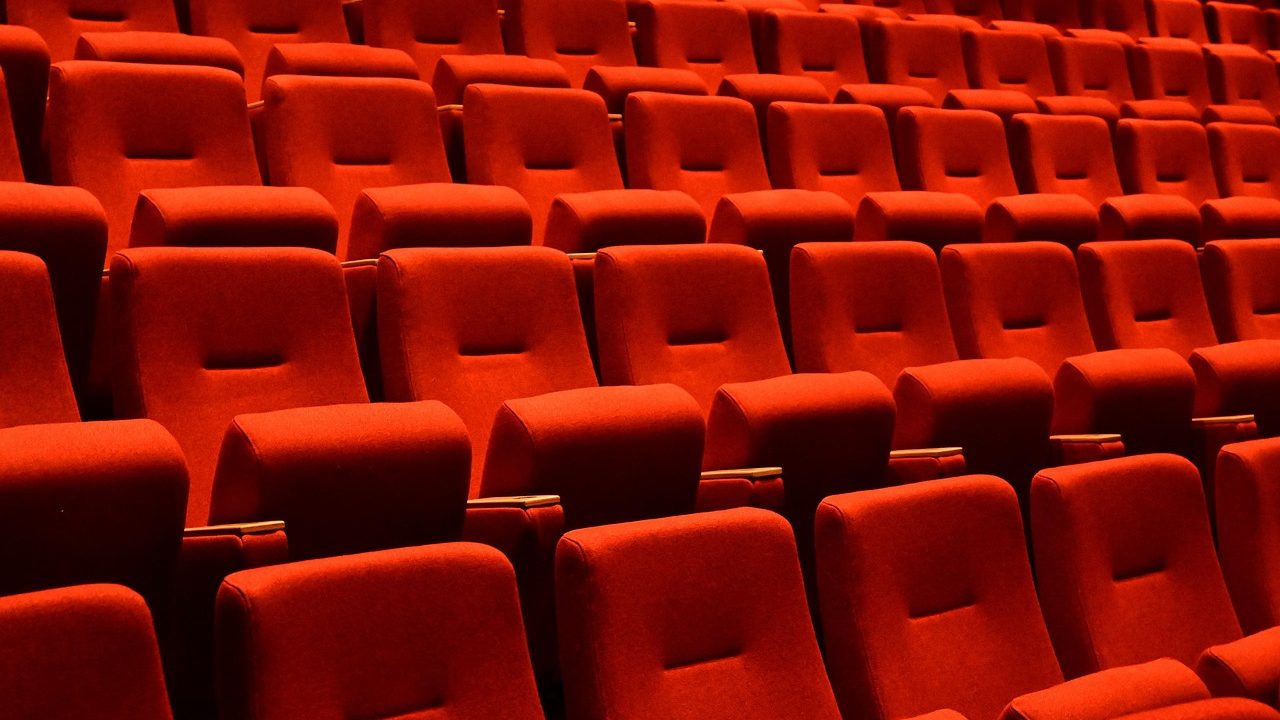 Rows of red velvet seats in an empty darkened movie theater.