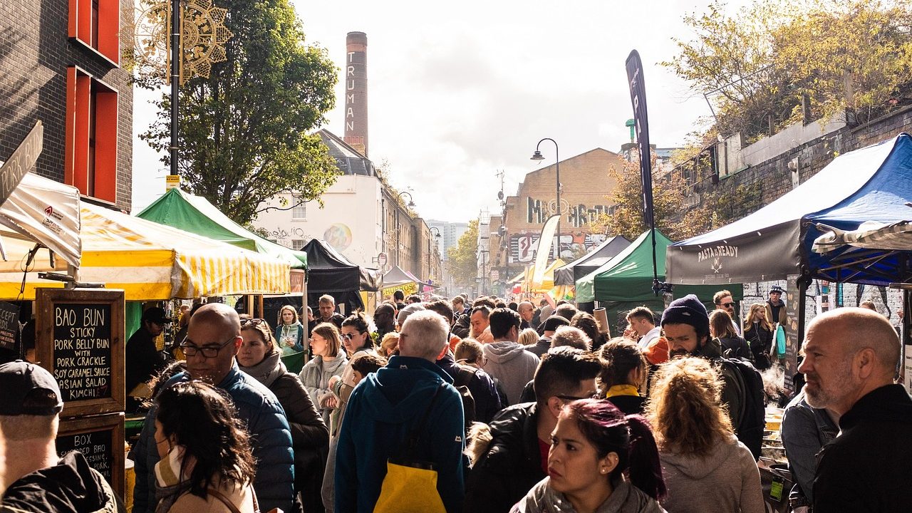 Colorful outdoor street festival with vendor tents and visitors walking along a closed urban avenue.